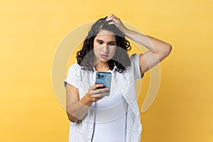 Pensive beautiful woman using cell phone thinking what to answer, keeps hand on head.