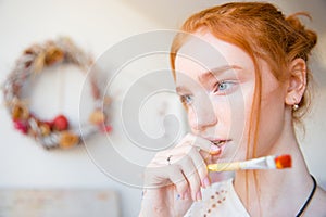 Pensive beautiful young female holding paintbrush and thinking