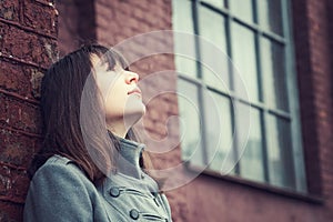 Pensive beautiful young girl standing near a brick wall