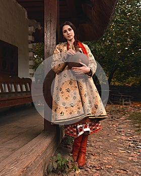 Pensive beautiful young woman dressed vintage traditional ukrainian embroidered clothes holding old crock in her hands
