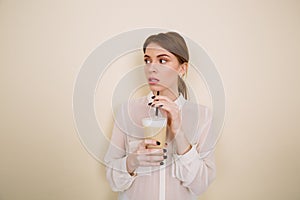 Pensive beautiful young woman standing and drinking coffee with milk