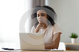 Pensive biracial woman thinking working on laptop