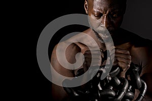 Pensive black man holding large heavy chains.