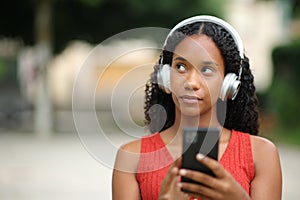 Pensive black woman listening audio in the street