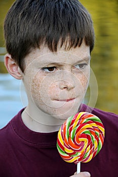 Pensive boy with freckles enjoys lolly