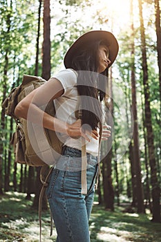 Pensive brave woman with backpack traveling alone among trees on outdoors. Young traveler girl hiking in forest