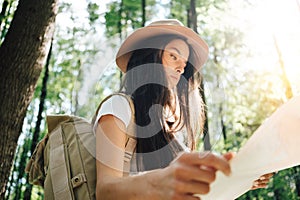 Pensive brave woman with backpack traveling alone among trees on outdoors. Young traveler girl hiking in forest and looking locati