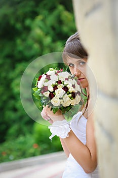 Pensive bride in white dress standing and holding roses bouquet