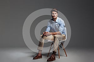 Pensive brunette man in blue shirt sitting on the chair