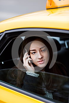Pensive brunette woman talking on phone sitting in yellow taxi