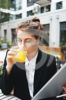 Pensive business woman in cafe sitting on veranda hold digital tablet and drinking juice