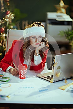Pensive business woman in green office with Christmas tree