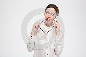 Pensive business woman talking on mobile phone and holding glasses