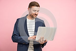 Pensive businessman with laptop isolated on pink wall working, types, chatting about work, business