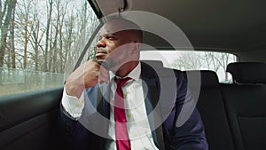 Pensive businessman riding in car backseat and looking out window