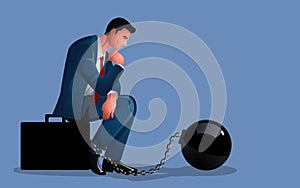 Pensive businessman seated upon a briefcase, shackled by the weight of an iron ball