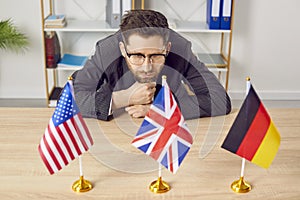 Pensive businessman sitting at desk looking at flags of different countries