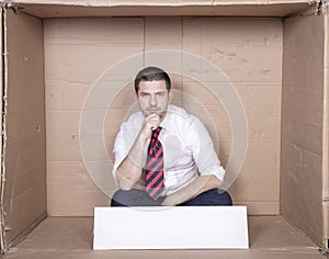 Pensive businessman sitting in a tight box, copy space on white blank board