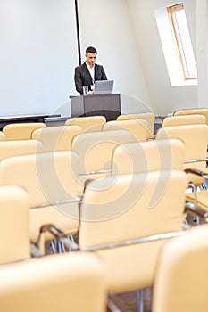 Pensive businessman standing and using laptop in empty meeting hall