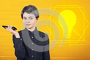 Pensive businesswoman holding mobile phone looking thinking of an innovative idea as light bulb symbol shining on yellow
