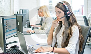 Pensive businesswoman talking on headset while working on laptop in office.