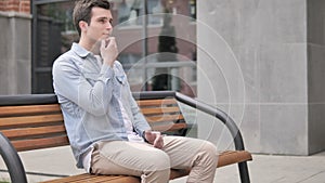 Pensive casual young man thinking while sitting outdoor
