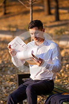 Pensive caucasian realtor in white shirt standing in park and reading documents from clipboard in his hands