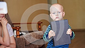 A pensive child holds a large black religious book in his hands, mom with closed eyes in the background