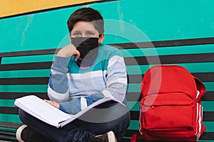 Pensive children in the park with a book and their mask on