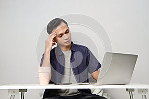 pensive confused asian man in the workplace whiile sitting in front of laptop computer. isolated background