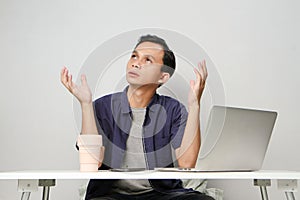 pensive confused asian man in the workplace whiile sitting in front of laptop computer. isolated background