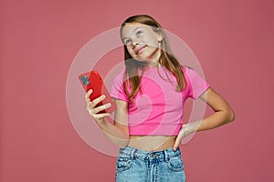 Pensive dreaming child girl hold phone looking up on pink background. Children gadget addiction. E-learning mobile apps