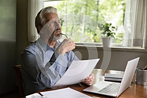 Pensive elderly male hold paper letter analyze information at workplace