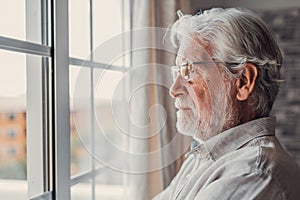 Pensive elderly mature senior man in eyeglasses looking in distance out of window, thinking of personal problems. Lost in thoughts