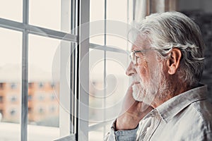 Pensive elderly mature senior man in eyeglasses looking in distance out of window, thinking of personal problems. Lost in thoughts