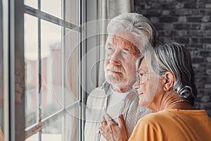 Pensive elderly mature senior man in eyeglasses looking in distance out of window, thinking of personal problems. Old woman wife