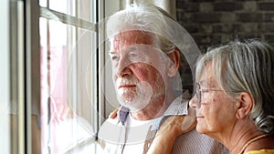 Pensive elderly mature senior man in eyeglasses looking in distance out of window, thinking of personal problems. Old woman wife