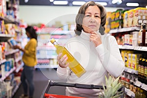 Pensive elderly woman choosing vegetable oil in supermarket