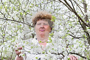 Pensive elderly woman in spring nature with cherry flowers