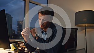 Pensive employee working night in office. Tired businessman checking hand watch