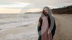 Pensive enigmatic woman walks along sea tides surf on sandy beach on autumn day. Fashionable mixed ethnic female in