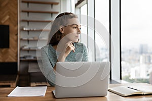 Pensive female employee work on laptop thinking