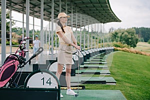 pensive female golfer in polo and cap with golf club looking away