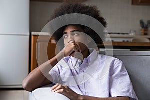 Pensive frustrated teenage African guy sitting on couch