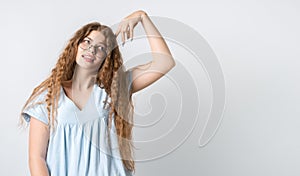 Pensive girl with curly long hair, and in round spectacles, looking up and holding her hand near head. Copy space