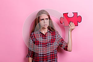 A pensive girl, holds a puzzle on her raised hand and looks at the shaft. On a pink background.