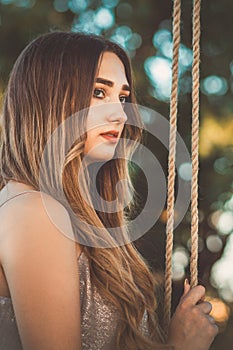 Pensive girl with long hair near rope swing on summer nature, young woman in loneliness, leisure activity, lifestyle concept