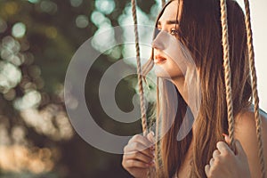 Pensive girl with long hair on rope swing on summer nature, young woman in loneliness, leisure activity, lifestyle concept