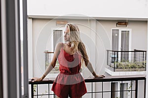 Pensive girl in pajama enjoying summer morning. Appealing long-haired woman standing at balcony