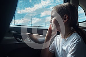 Pensive girl sits in car on backseat feeling sadness